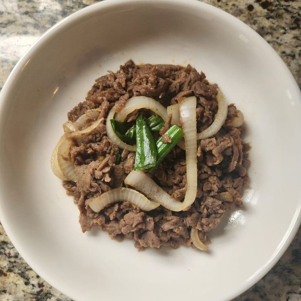 A white bowl filled with Korean bulgogi, topped with sliced onions and green onions.