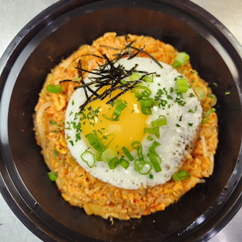 Kimchi fried rice topped with a fried egg, green onions, and shredded nori in a black bowl.