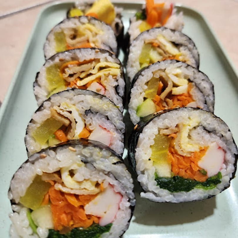 Close-up of several slices of Korean gimbap with various colorful fillings on a light green tray.