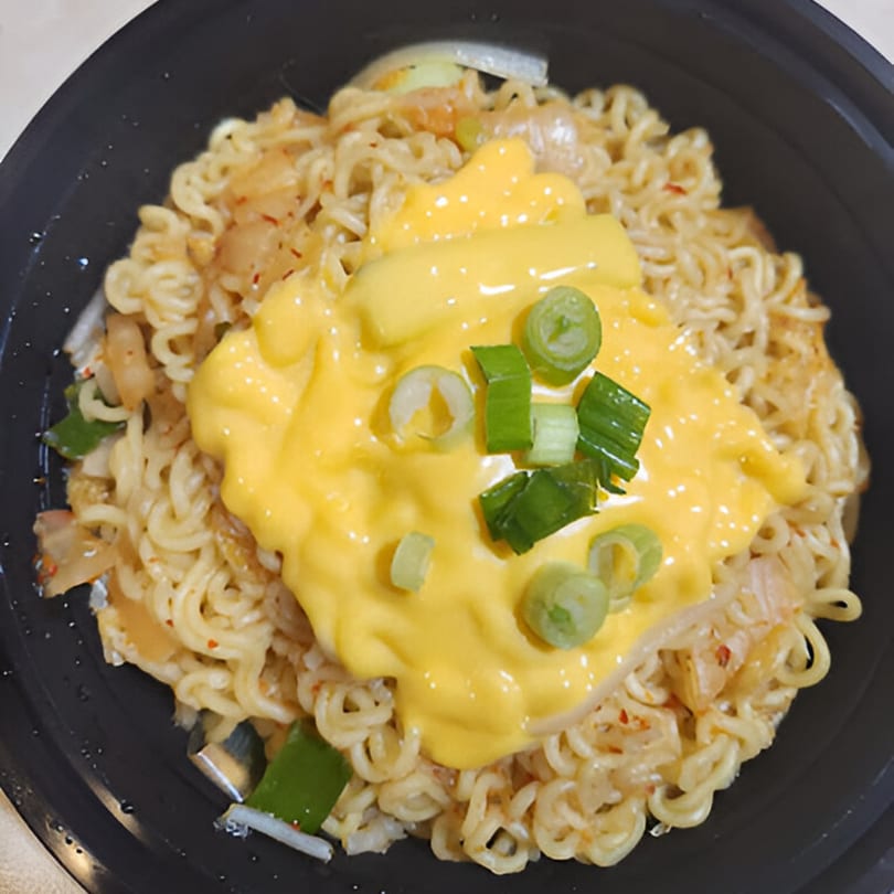Korean ramen noodles topped with melted cheese and chopped green onions in a black bowl.